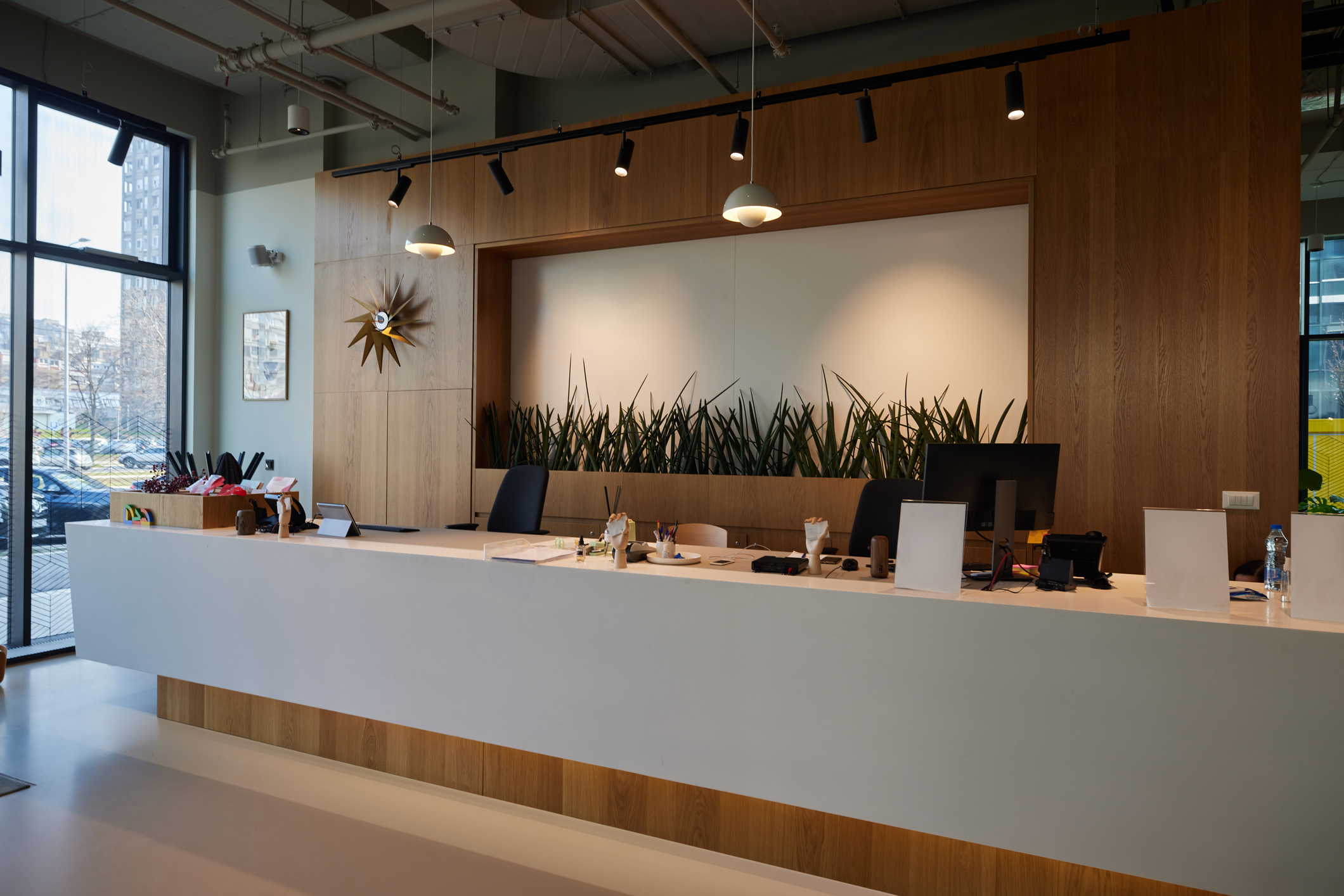 A long modern office reception with a combination of wood panels and white  vinyl, illuminated by various light sources